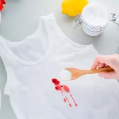 Biała koszulka z plamą krwi, soda oczyszczona na łyżce, cytryna, ocet i butelka z płynem.