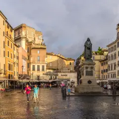 Campo de' Fiori, Rzym. Po deszczu, na mokrym bruku placu, ludzie spacerują obok pomnika.