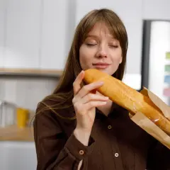 Kobieta wącha świeżą bagietkę, zastanawiając się, jakie choroby powoduje gluten.