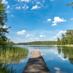 Drewniany pomost prowadzi do spokojnego jeziora w Drawieńskim Parku Narodowym. Otoczone zielenią, z błękitnym niebem i białymi chmurami.