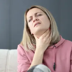 Kobieta z bólem ściska gardło, cierpiąc na porażenie strun głosowych.