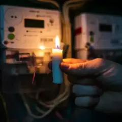 Gdy najemca nie płaci czynszu, można odłączyć mu media. Płonąca świeca w dłoni na tle liczników energii elektrycznej symbolizuje brak prądu.