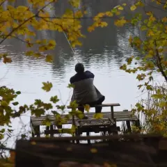 Jesień nad jeziorem. Mężczyzna siedzi na pomoście, łowiąc ryby. To jego pierwszy egzamin na kartę wędkarską.