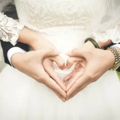 Dłonie tworzą serce na tle sukni ślubnej. To symbol miłości i tradycyjne błogosławieństwo na nowej drodze życia.