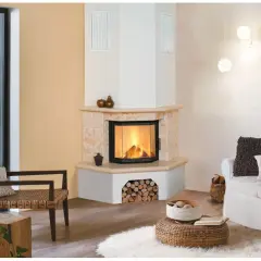 Gemütliches Wohnzimmer mit einem Eck-Kachelofen, der einladend brennt. Ein Rattansessel und ein weißes Sofa laden zum Entspannen ein.