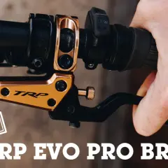 A hand squeezes a black brake lever on a bicycle handlebar. The gold TRP EVO PRO BRAKES are featured in this review.