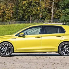 Żółty hatchback stoi na tle zieleni i drzew.