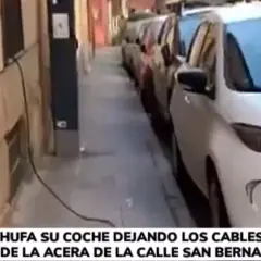 Un coche eléctrico en carga, con cables cruzando la acera, obstaculizando el paso.
