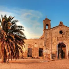 El cortijo del fraile, una edificación antigua con una palmera imponente, bajo un cielo azul y nubes al atardecer.