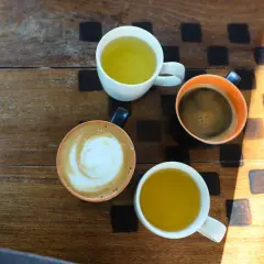 Kawa i herbata na drewnianym stole. Czy zielona herbata pobudza? Obok kawy latte i espresso, dwie filiżanki zielonej herbaty.