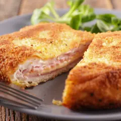 Złocisty kotlet po szwajcarsku, przekrojony na pół, odsłaniający soczyste mięso, szynkę i ser. Podany z zieloną sałatką.