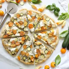 Gesunder pizzateig mit Zucchini, Kirschtomaten und Mozzarella, garniert mit Basilikum und Zucchiniblüten.