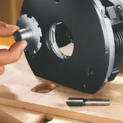 Main d'un artisan ajustant un accessoire sur une défonceuse, pour un choix précis de l'outil. Bois et fraise à portée de main.