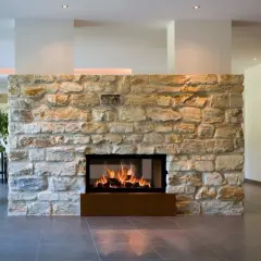 Un moderno embellecedor chimenea de piedra rústica con fuego encendido. A la izquierda, una planta grande. A la derecha, una estantería de madera.