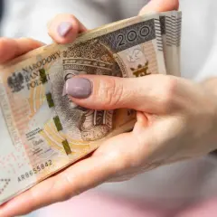 Dłonie trzymające stos banknotów 200 zł. Czas oczekiwania na wypłatę emerytury po złożeniu wniosku.
