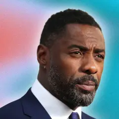 Idris Elba arbore une barbe grise stylée, un modèle barbe dégradé impeccable, sur fond dégradé rouge et bleu.