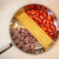 Zutaten für ein schnelles One-Pot-Gericht: Spaghetti, gehackte rote Zwiebeln, Kirschtomaten und Knoblauch in einer Pfanne.