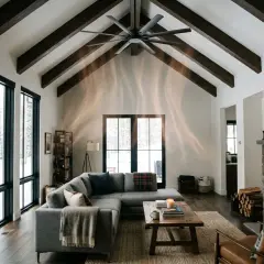 Salon cosy avec cheminée en pierre, canapé gris, grandes fenêtres donnant sur la neige. Le **chauffage au plafond** discret assure une chaleur douce.