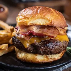 Gros plan sur un burger maison avec bacon, fromage fondant et frites croustillantes sur une assiette noire.