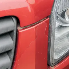 Pęknięty lakier na czerwonym zderzaku obok reflektora. Zastanawiasz się, ile kosztuje pomalowanie auta?
