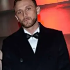 Kamil Nożyński z partnerką na ściance. Elegancki garnitur i czerwona sukienka.