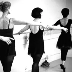 Three women in black leotards practice ballet at a barre.