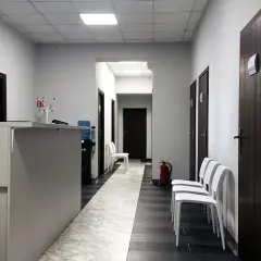 Korytarz centrum medycznego z recepcją, drzwiami i białymi krzesłami.