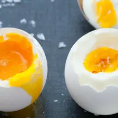Dwa jajka na miękko z płynnym żółtkiem, jedno na łyżce, obok sól.