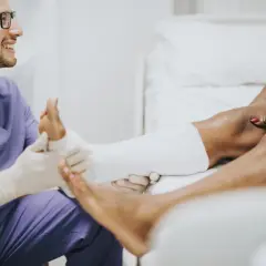 Medico sorridente applica una fasciatura a un paziente con un malleolo gonfio.