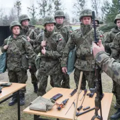 Żołnierze w mundurach ćwiczą, co zabrać na ćwiczenia rezerwy. Na stołach broń, magazynki, nóż i torby.