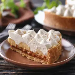 Rebanada de tarta banoffee con plátano, dulce de leche y crema batida, espolvoreada con canela.
