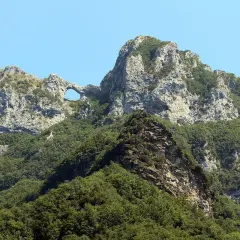 Il monte forato, con la sua roccia scolpita dal vento, si erge maestoso tra il verde della vegetazione e l'azzurro del cielo.