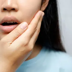 Mujer con mano en la mejilla, experimentando dolor de dientes al quitar Invisalign.