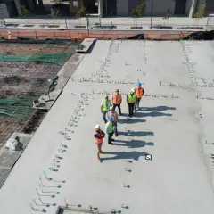 Grupa budowlańców na placu budowy, gdzie widać zbrojenie i świeży beton. Zastanawiają się, ile kosztuje metr betonu na fundament.