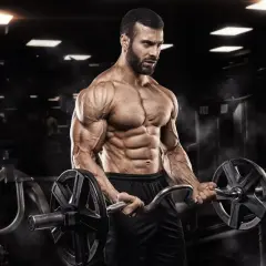 Mężczyzna z wyrzeźbionymi mięśniami wykonuje ćwiczenia na biceps z łamaną sztangą w siłowni.