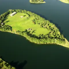 Ostrów Lednicki, zielona wyspa na jeziorze, otoczona drzewami, z widocznymi budynkami i fragmentami ruin.