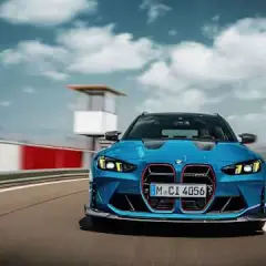Niebieskie BMW M3 Competition pędzi po torze wyścigowym, chmury na niebie dodają dynamiki.