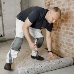 Bauarbeiter rollt Dämmmaterial aus. Gute eurokristall erfahrungen sind wichtig für die Isolierung.