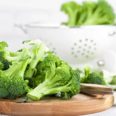 Brocolis frais coupés sur une planche en bois, prêts pour une recette saine. Un égouttoir blanc est visible en arrière-plan.