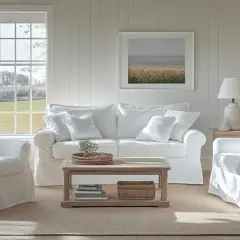 Gemütliches Wohnzimmer im **New England Style** mit weißen Sofas, Sesseln, Holztisch und einem Bild mit Meeresmotiv.