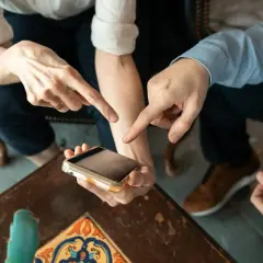 Dwie osoby wskazują palcami na ekran telefonu, dyskutując, ile kosztuje aplikacja.