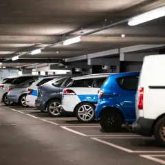 Montaż czujników parkowania w garażu podziemnym. Rzędy samochodów, w tym biała furgonetka, niebieski hatchback i kilka innych pojazdów, stoją na miejscach parkingowych.