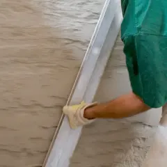 Hand mit Handschuh glättet feuchten Putz. Spezialputz gegen Feuchtigkeit schützt die Wand.