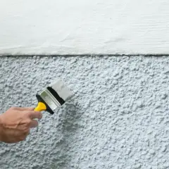 En hand målar en vägg utomhus. Temperaturen är perfekt för att måla, inte för varmt eller kallt.