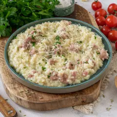Cremiges Risotto mit Salsiccia, garniert mit Parmesan und Petersilie, serviert auf einem rustikalen Holzbrett.