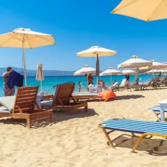 Słoneczny dzień na plaży Naxos. Leżaki pod parasolami, turkusowa woda i góry w tle.