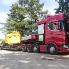 Czerwony Scania z naczepą transportuje żółtą koparkę. To typowa przesyłka dużych gabarytów, gotowa do drogi.
