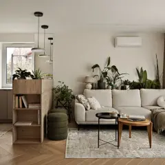 Jasny salon w stylu minimalistycznym z dużą ilością roślin. Jasna kanapa, drewniane meble i subtelne dodatki tworzą przytulną atmosferę.