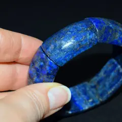 Dłoń trzyma bransoletkę z lapis lazuli, kamienia o intensywnym niebieskim kolorze i złotych inkluzjach.