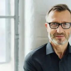 Man med glasögon och skägg, klädd i svart skjorta. Perfekt för bra profilbilder som ger ett professionellt intryck.